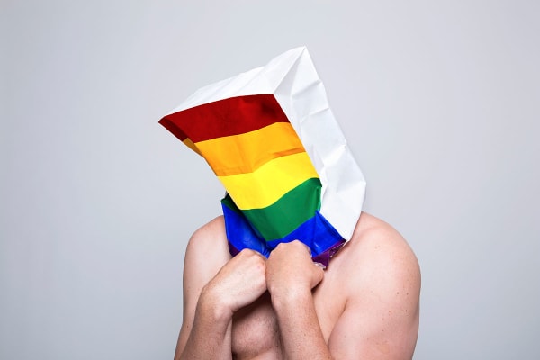 Photograph of a man wearing a paper bag with the LGBT rainbow flag on it by Christa Holka