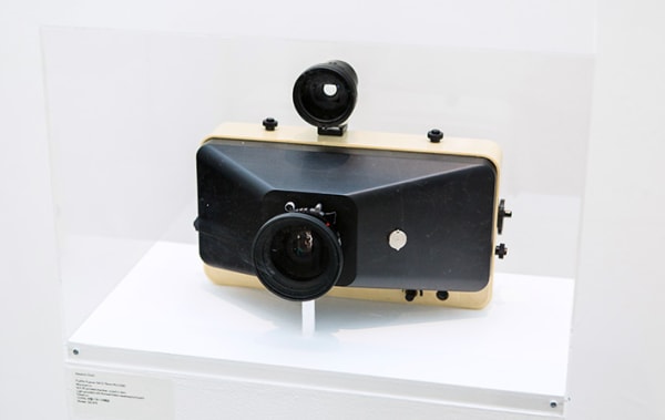 A vintage camera enclosed in a transparent box atop a plinth.