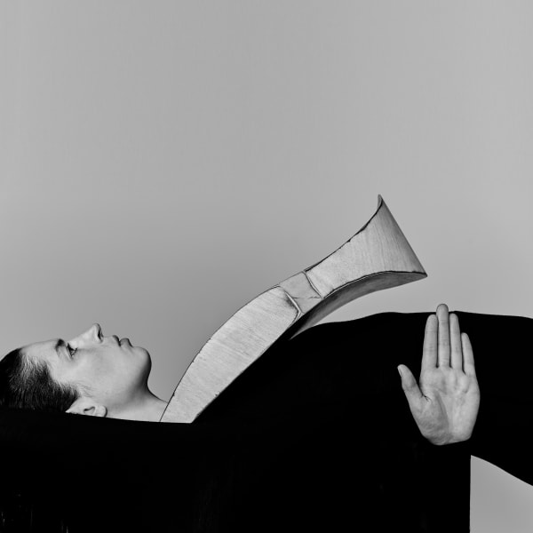 Black and white image of model on their back with extra large accessory on their nexk