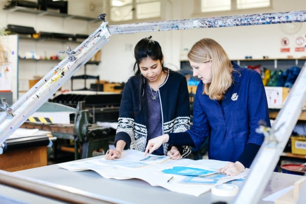 Two women standling at a screen printing bed discussing student's work