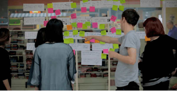 Four people in front of a wall full of sticky notes.