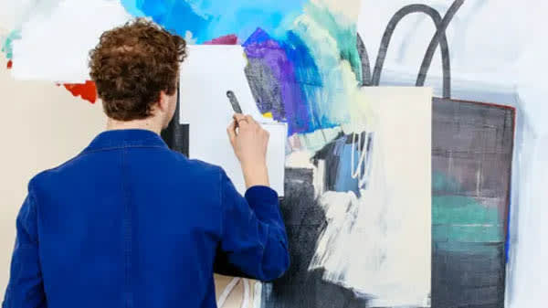 A student with his back to the camera, is creating an abstract painting 