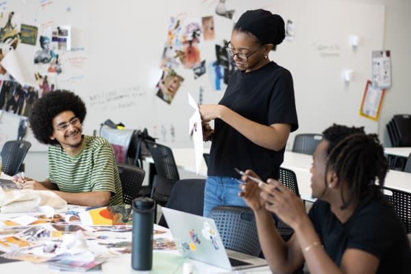 3 people at a table smiling and chatting while drawing and cutting paper