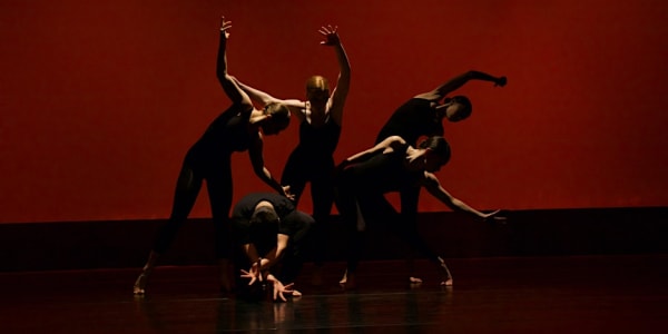 Five dancers on stage with red backdrop.