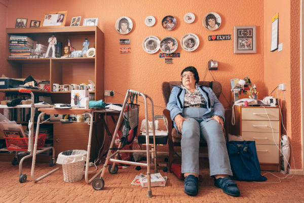 Portrait of an older woman sitting in her armchair surrounded by her belongings.