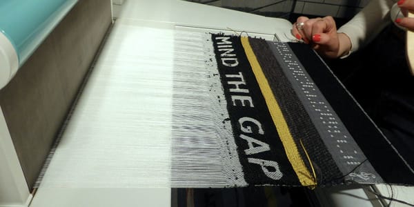 A fabric being woven on a loom that reads 'MIND THE GAP