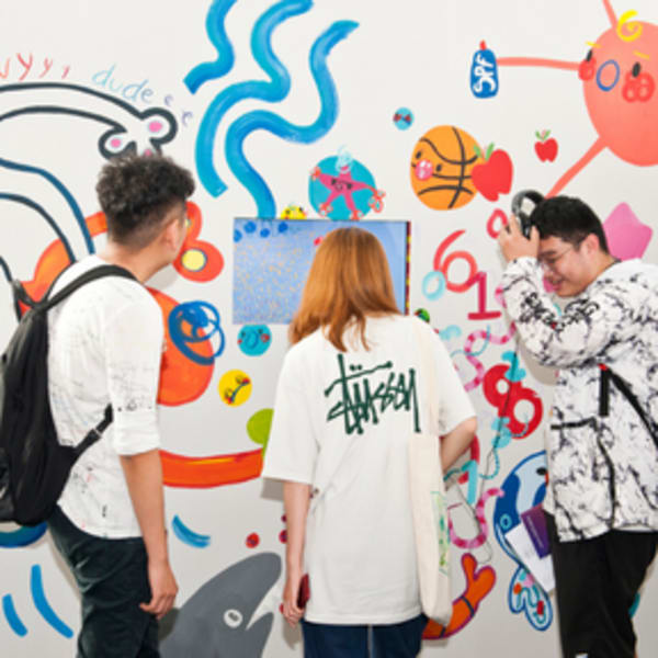 three students stand in front of colourful artwork