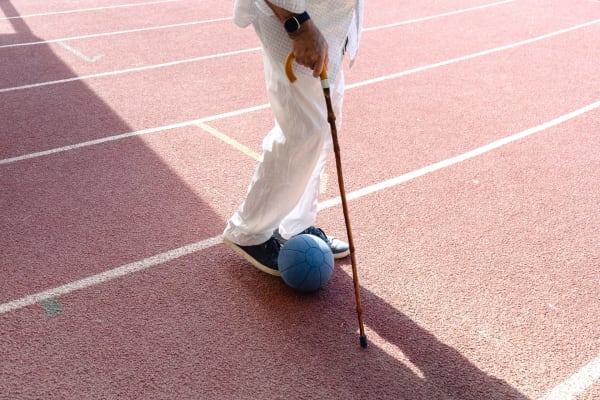 Photograph of a pink sports court with a figure's leg's, feet and walking stick standing beside a ball.