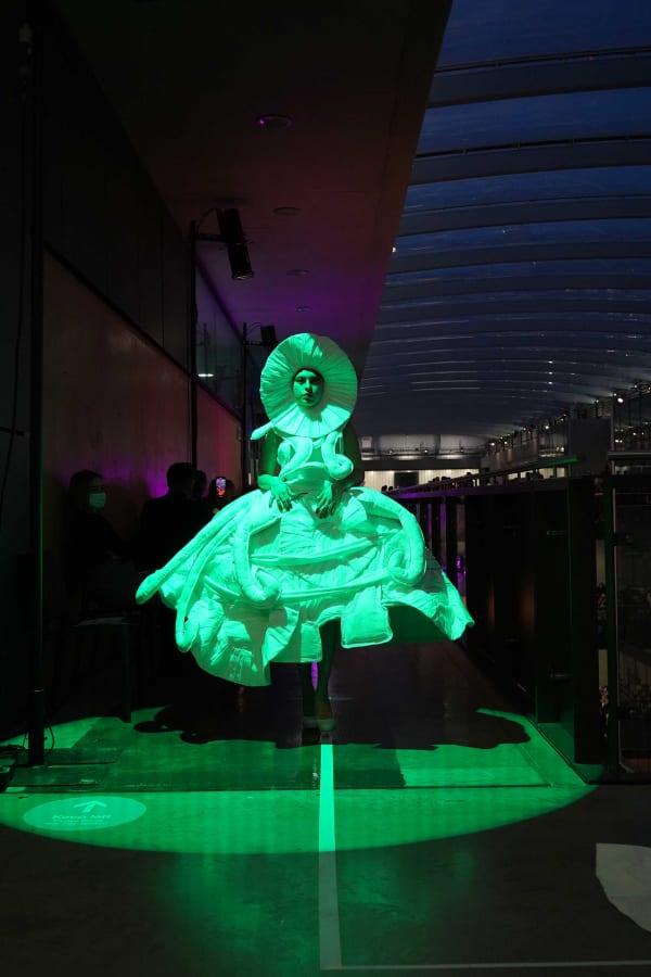 Figure wearing wight garments  walking down green lit pathway