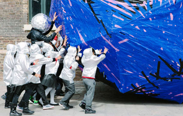 Children in white boiler suits pushing large blue ball