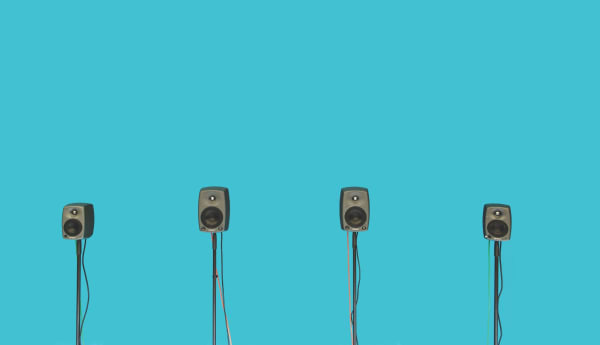 Four speakers on stands, in front of solid light blue background.