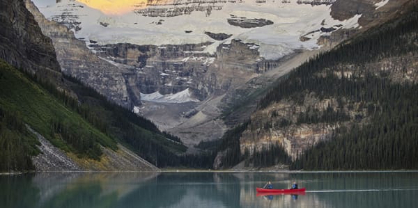 Photo of a red canoe with two people in on the water of Lake Louise in Aberta, Canada with mountains surrounding