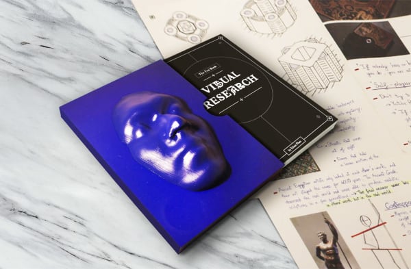 Black visual research publication coming out of blue cover with 3D face on, sitting next to annotated research.