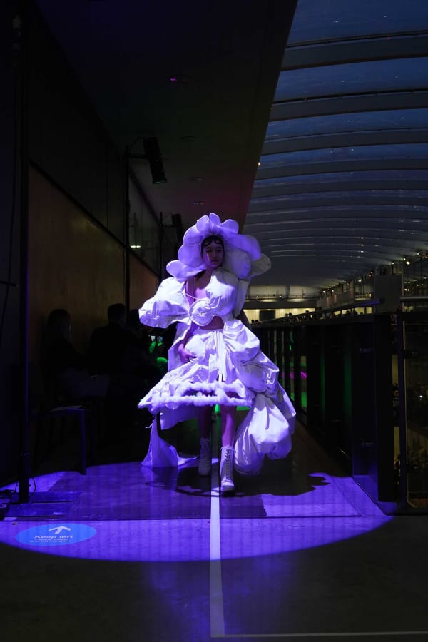 Figure wearing wight garments  walking down purple lit pathway