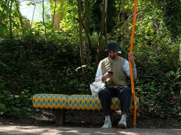 A person sat on an upholstered bench holding an orange pole