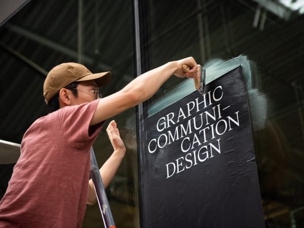 A person pasting a sign that reads Graphic Communicaiton Design to a window 