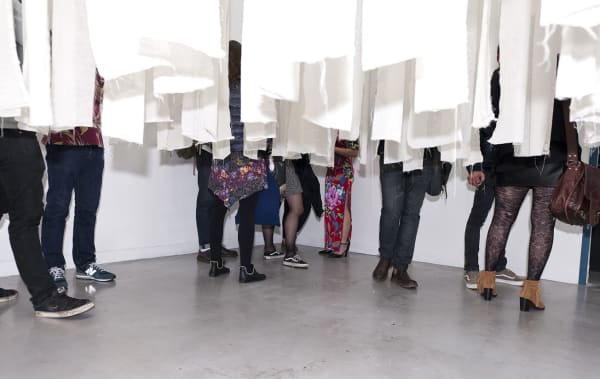 People standing inside an installation of white strips of paper hanging from the ceiling