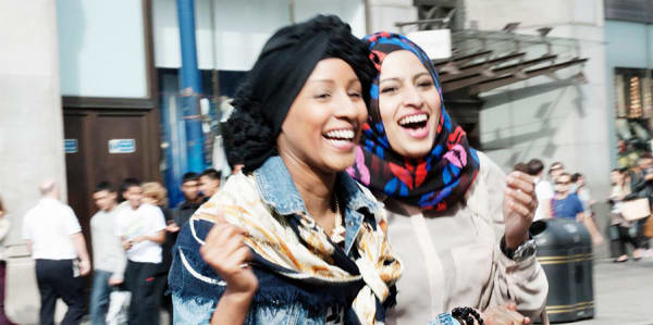 2 young girls wearing headscarves walking on the high street and laughing