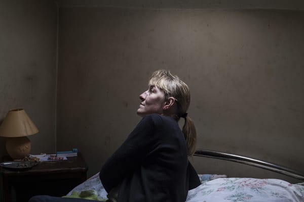 Photograph of a woman with blonde hair in a dark bedroom