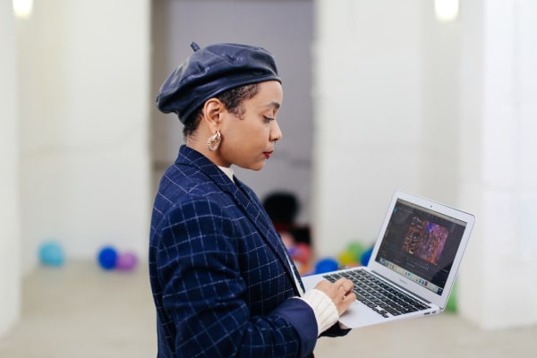 A young woman in a beret and matching jacket, typing on her laptop