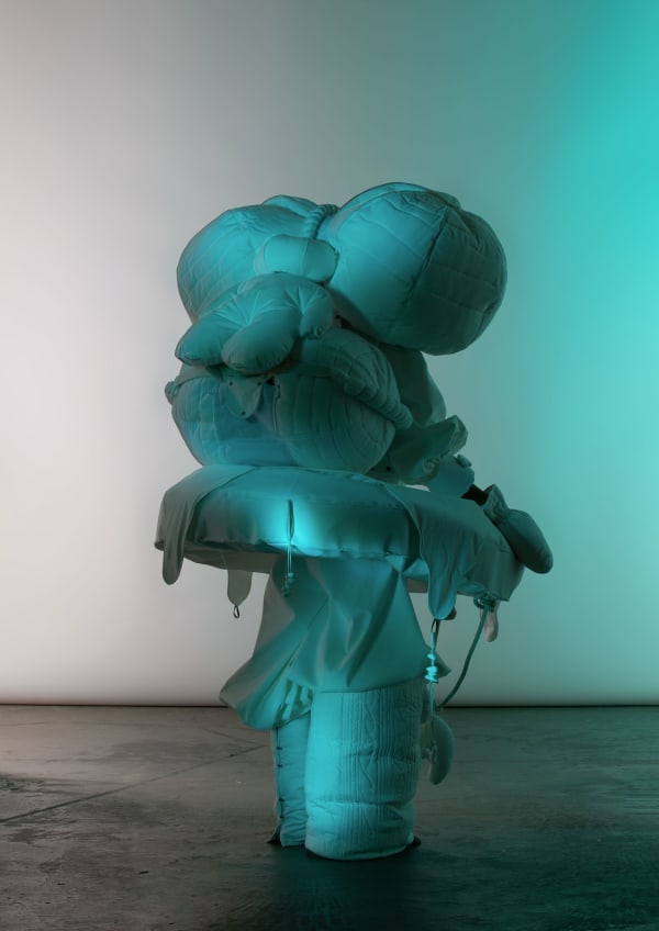 Figure wearing multiple voluminous white garments lit in green/blue