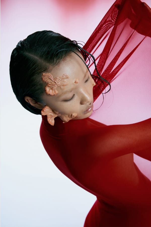 A model with prosthetic facial additions poses in a red outfit