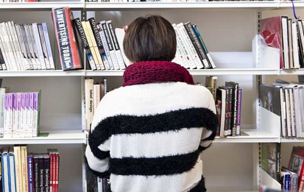 Photo of the back of a person wearing a black and white stripy jumper standing in front of a bookshelf