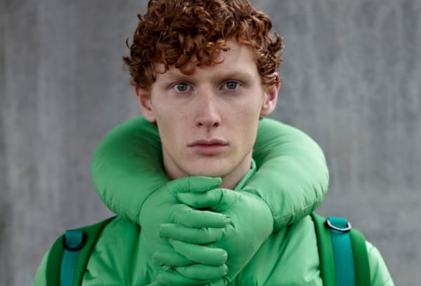 Red-haired model in turquoise padded coat with interlaced fingers