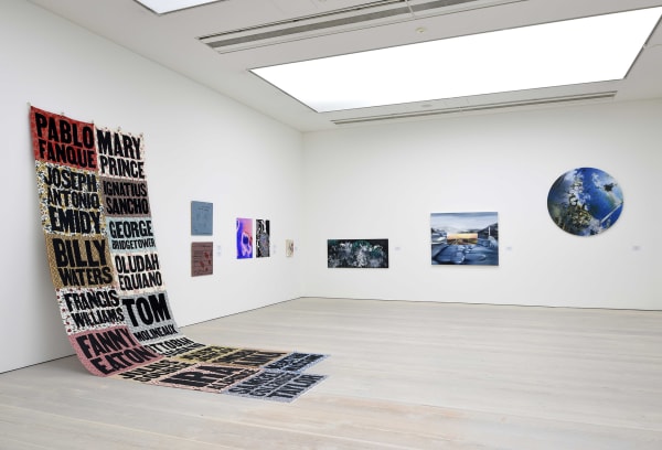 Installation view of several paintings and one large quilt hung on white wall