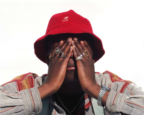 Man in red hat covers his face with hands. He is wearing rings.