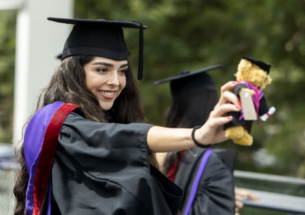 Student wearing cap and gown and holding a small teddy bear
