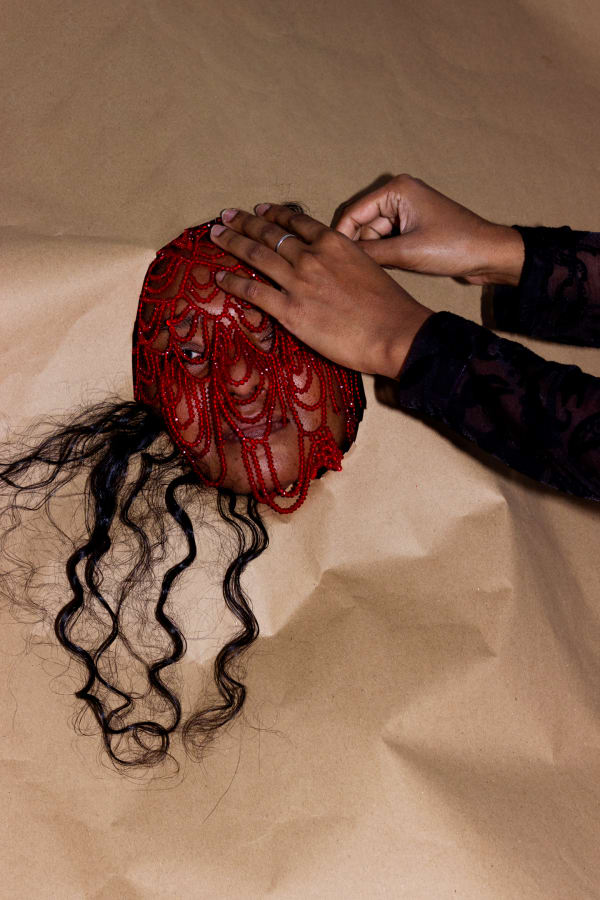 A person wearing a red beaded mask with their head surrounded by brown paper