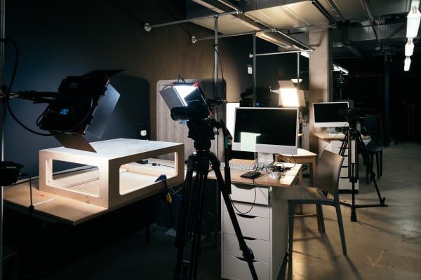 Workstations in the animation studio. Each has lights, pedestal of drawers, keyboard and screens. There are chairs and tripods by some of the workstations.