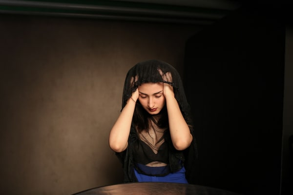 Woman in a dark room holding her head in her hands