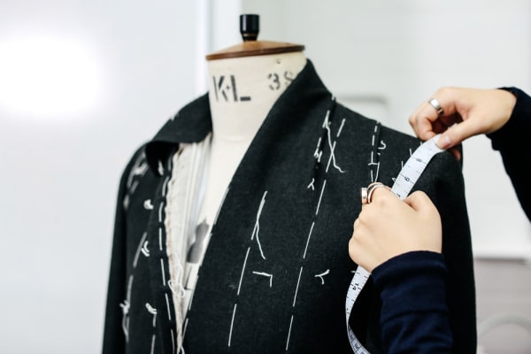 Close up shot of a student taking measurements of a black suit on a mannequin.