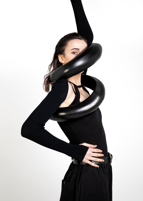 Female model wearing a thick black scarf made of plastic in an attempt to shield from crowds.