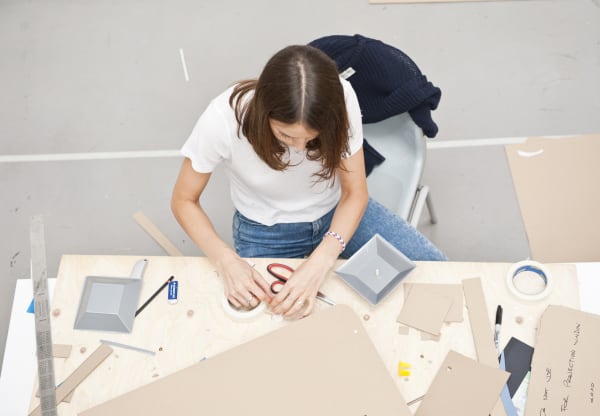 View down to a student seated at a desk and using various tool and cardboard materials. 