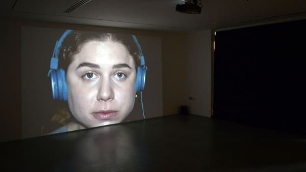 Video projection at Camberwell Space showing a close up shot of a girl with headphones on.