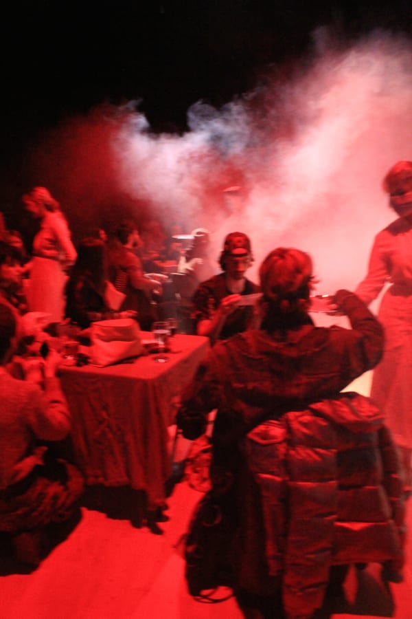 People sittign and standing in a red-lit room full of dry ice
