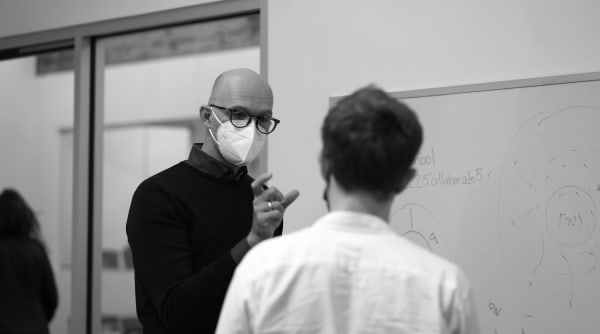 man in protective mask gestures to a student