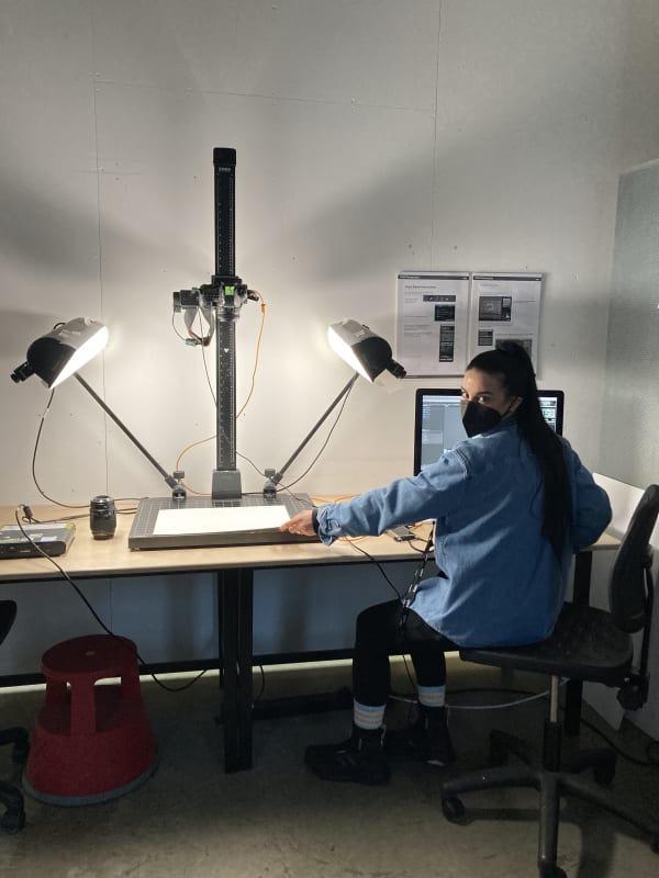 A person sat using a photography copy stand. They are facing the camera and wearing a mask