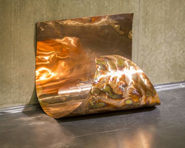 a piece of curled bronze sheet metal with light reflecting off the surface. 