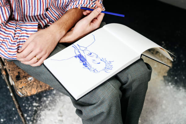 A person sat with their hands crossed on their lap, holding a pen and sketchbook.