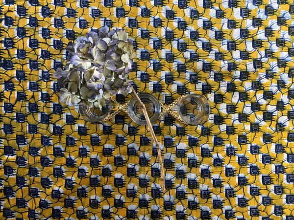Flowers, drinking glasses and gold chains arranged and shot from above against a vivid patterned mustard, white and black background. 