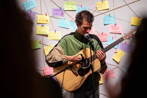 Musician playing a guitar in front of wall with colourful notes.