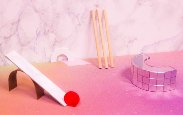 Various small objects arranged on a pink bench next to a marble effect background. Includes mirror tiled rainbow curve, seesaw with a red pompom and three wooden rods.