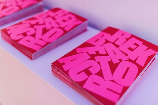 piles of BREAKFACTOR exhibition guides on a counter. designed on red card with pink block capital stylised font and letters displaced across the page.