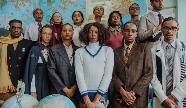 classroom photo of 13 Black models in various uniforms and formalwear. In the background walls of maps, and in front two globes.
