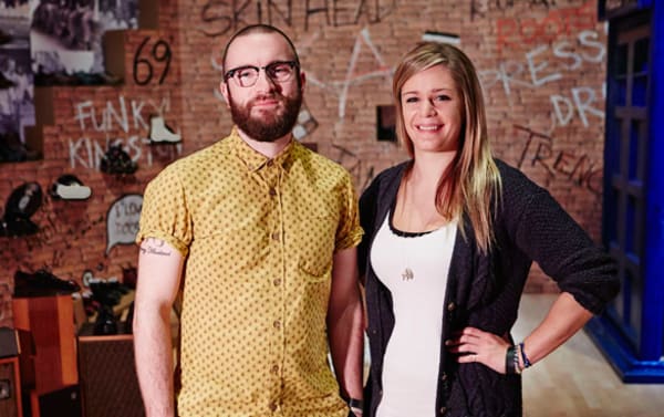 Two people standing next to each other in front of  a brick wall