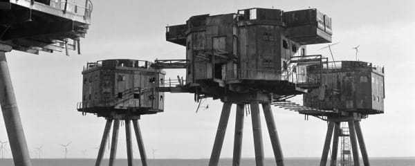 Greyscale photograph of brutalist concrete structures on stilts the water.
